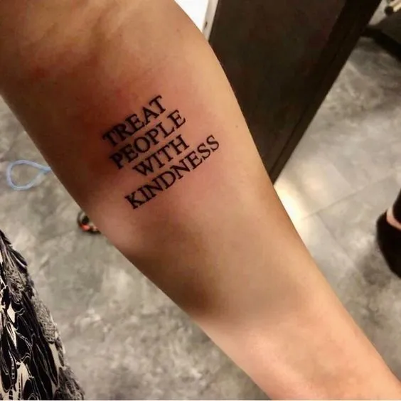 Hình xăm chữ tiếng Anh "Treat people with kindness" trên cánh tay, thể hiện lòng tốt
